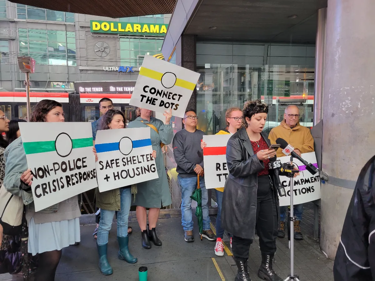 People with protest signs and a speaker by a building