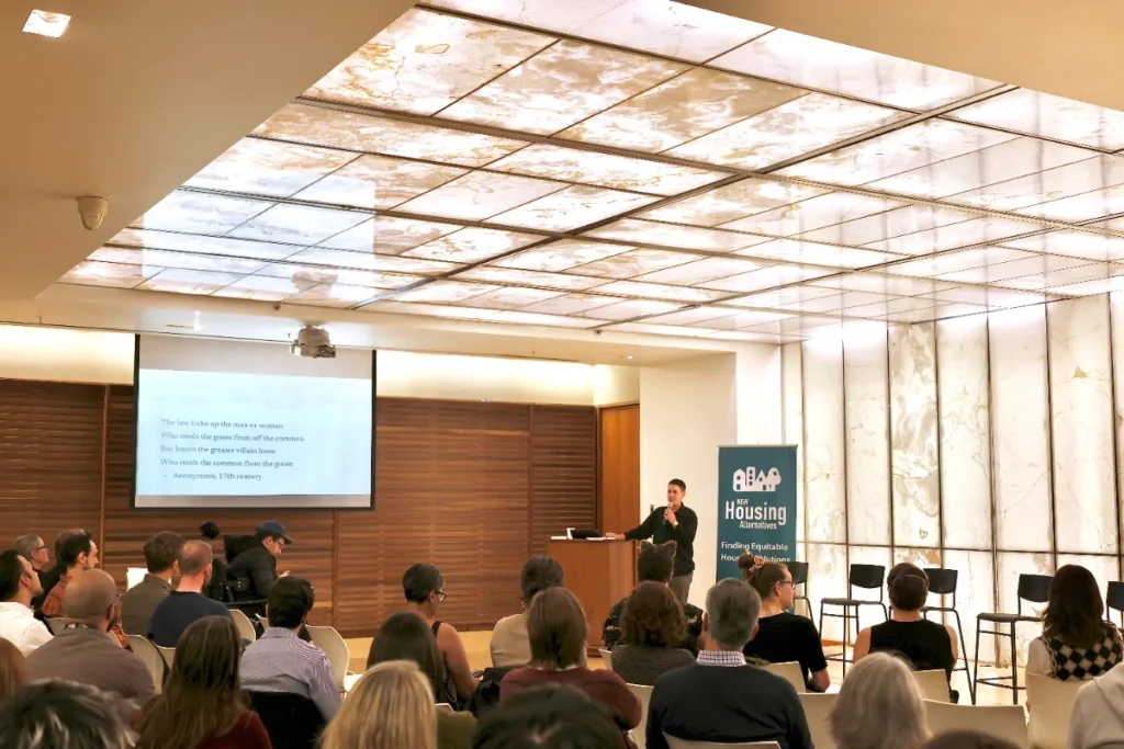 A seated room with speaker up front by lit panels