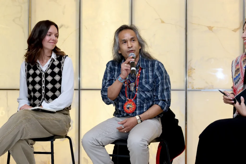 A panel speaker holding a mic and wearing a red indigenous pandant