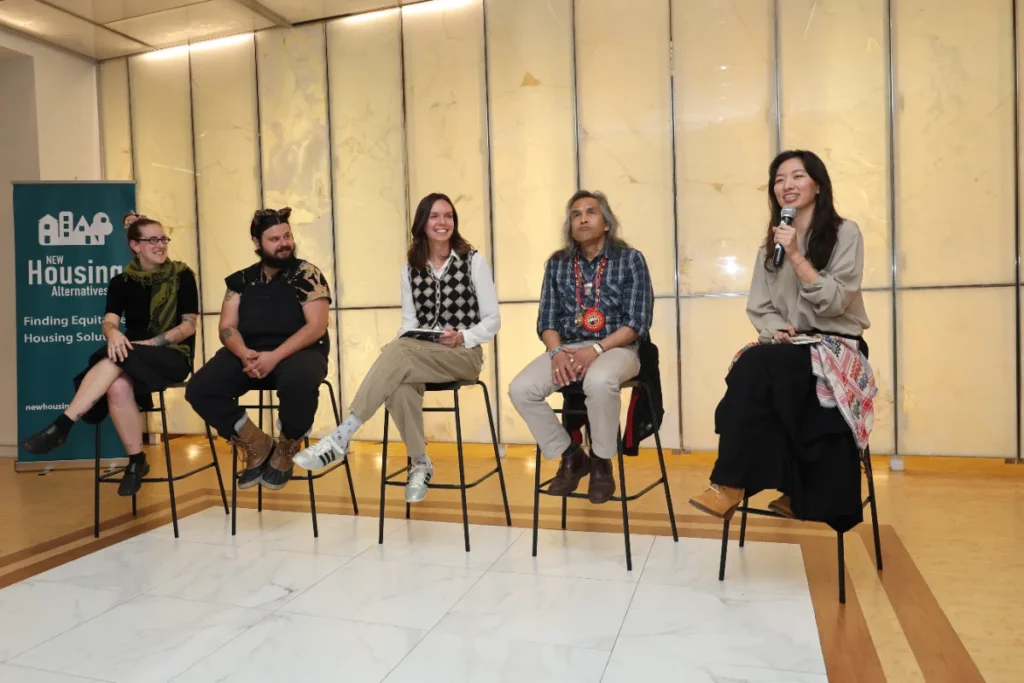 A panel speaker holding a mic, with other panel speakers listening