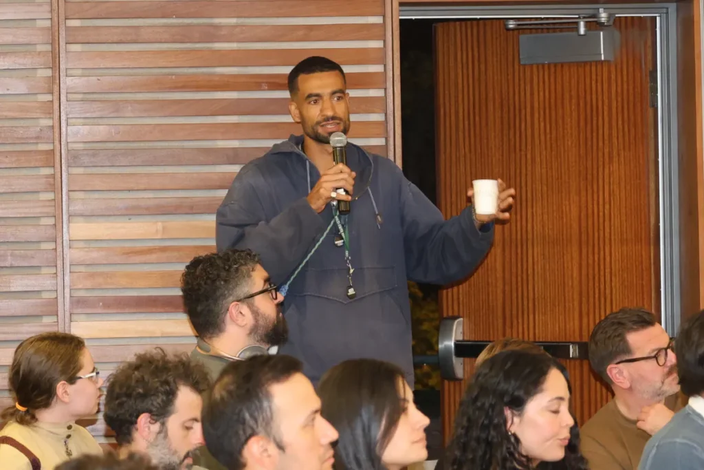 A tall man speaks with a microphone ad a cup